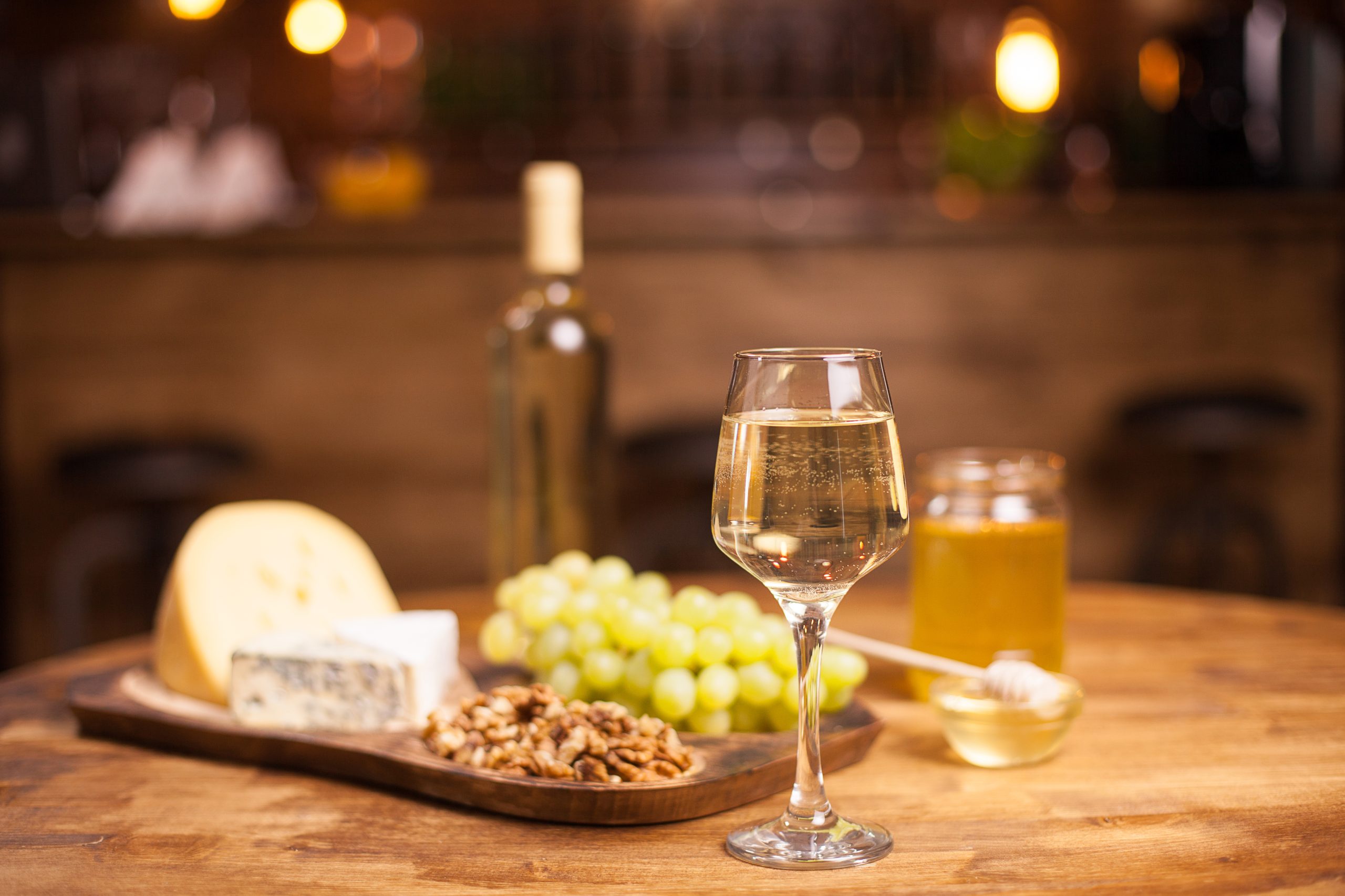 A glass of white wine with cheese and grapes on a wooden table
